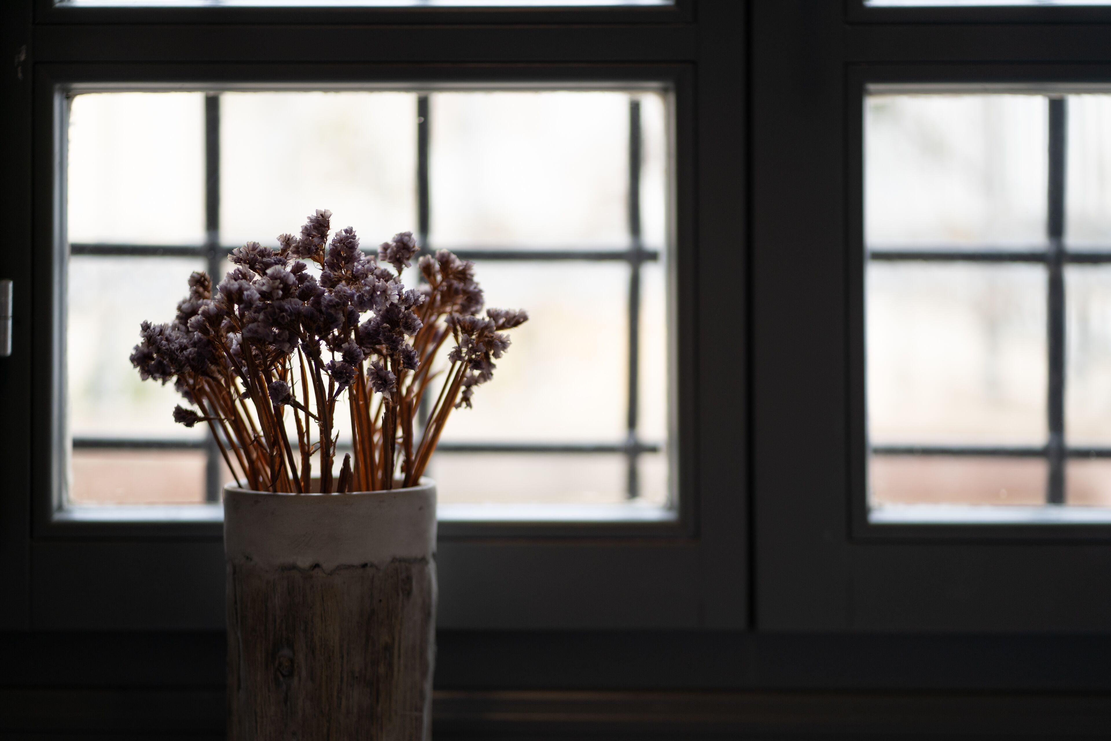 Eine rustikale Vase mit getrockneten Blumen auf einem Fensterbrett.
