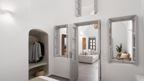A modern, minimalist room with a built-in wardrobe, a large mirror, and a cozy seating area with a sofa and chairs. - Kastro Mansion (Santorini)