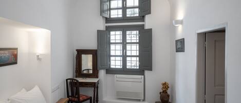 A bedroom with a bed, a desk, a chair, a window with shutters, a radiator, and a door.