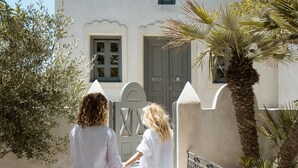 Two people walking up a stone staircase to a white building with a door and windows. - Kastro Mansion (Santorini)