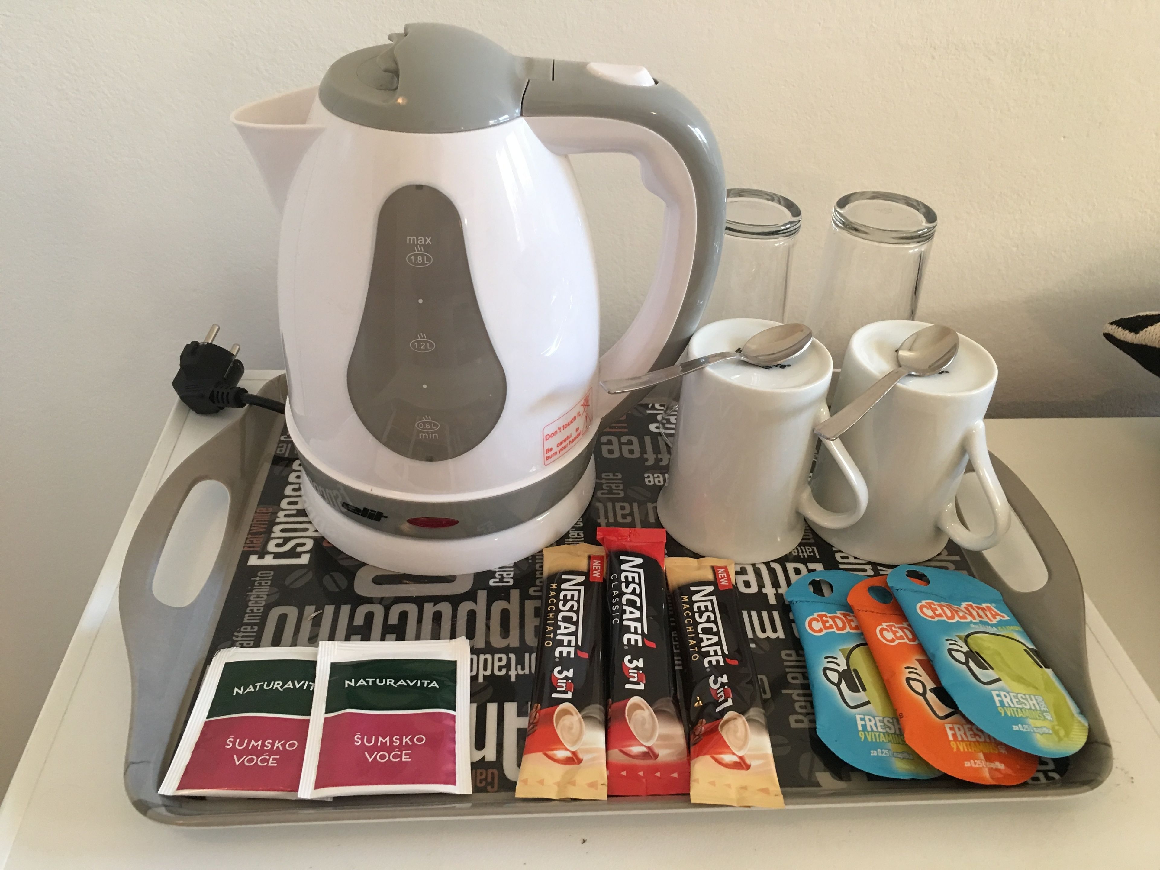 A tray with a coffee maker, two cups, two glasses, and packets of coffee and tea.
