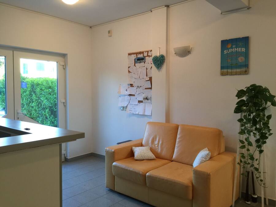 Una habitación con un sofá color beige, una pizarra con notas, una ventana y una planta.