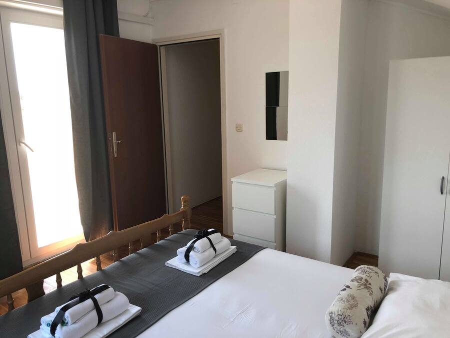 Une chambre d’hôtel avec un lit, une table de chevet avec des serviettes, une armoire, un petit meuble blanc et un miroir au mur.