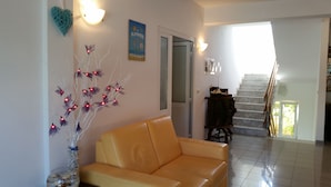 A living room with a yellow sofa, a decorative light fixture, and a staircase leading to another level. - Apartmani Ana&Ita (Novalja)