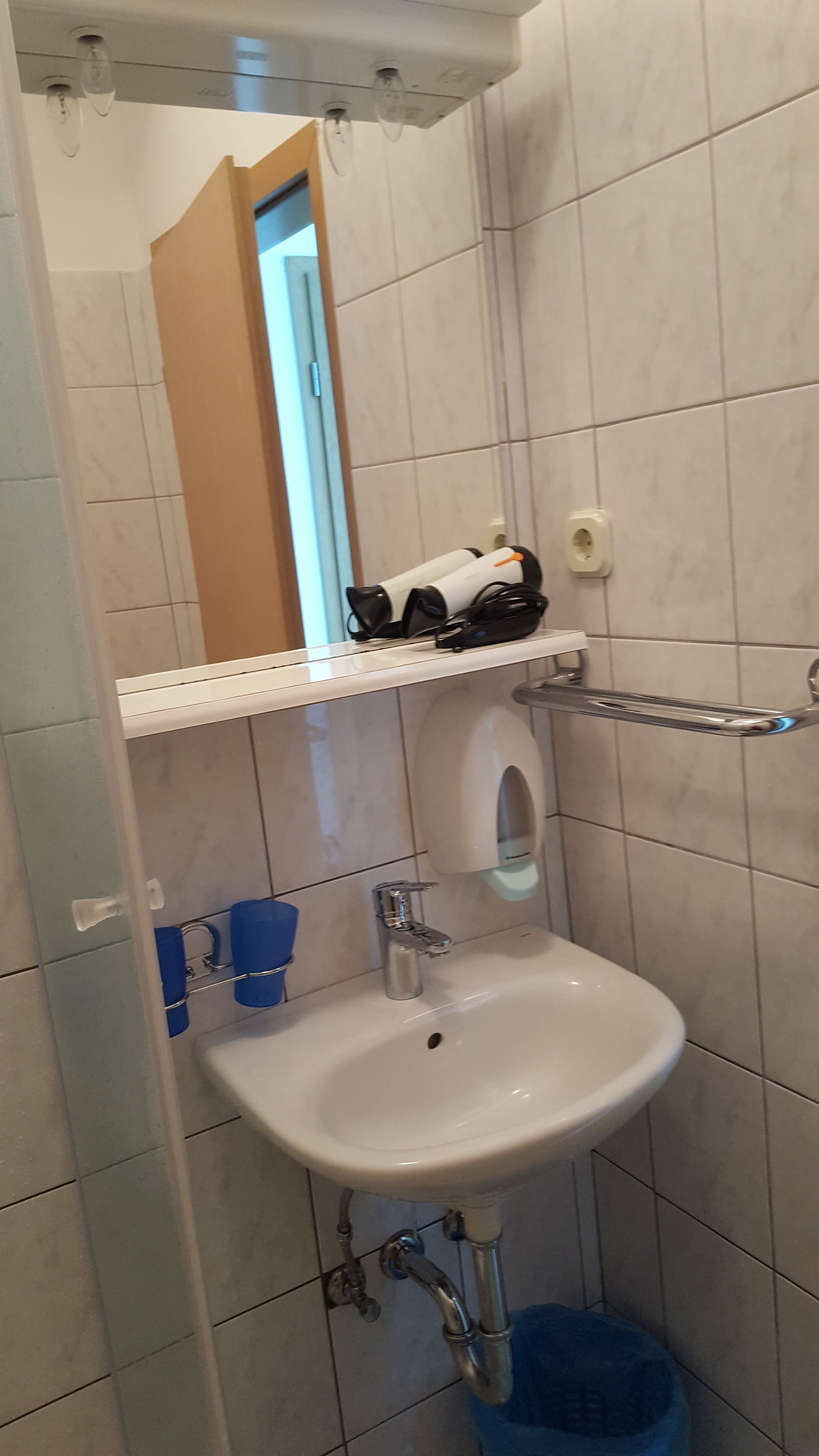 A bathroom with a white sink, a mirror, and a shelf with toiletries.