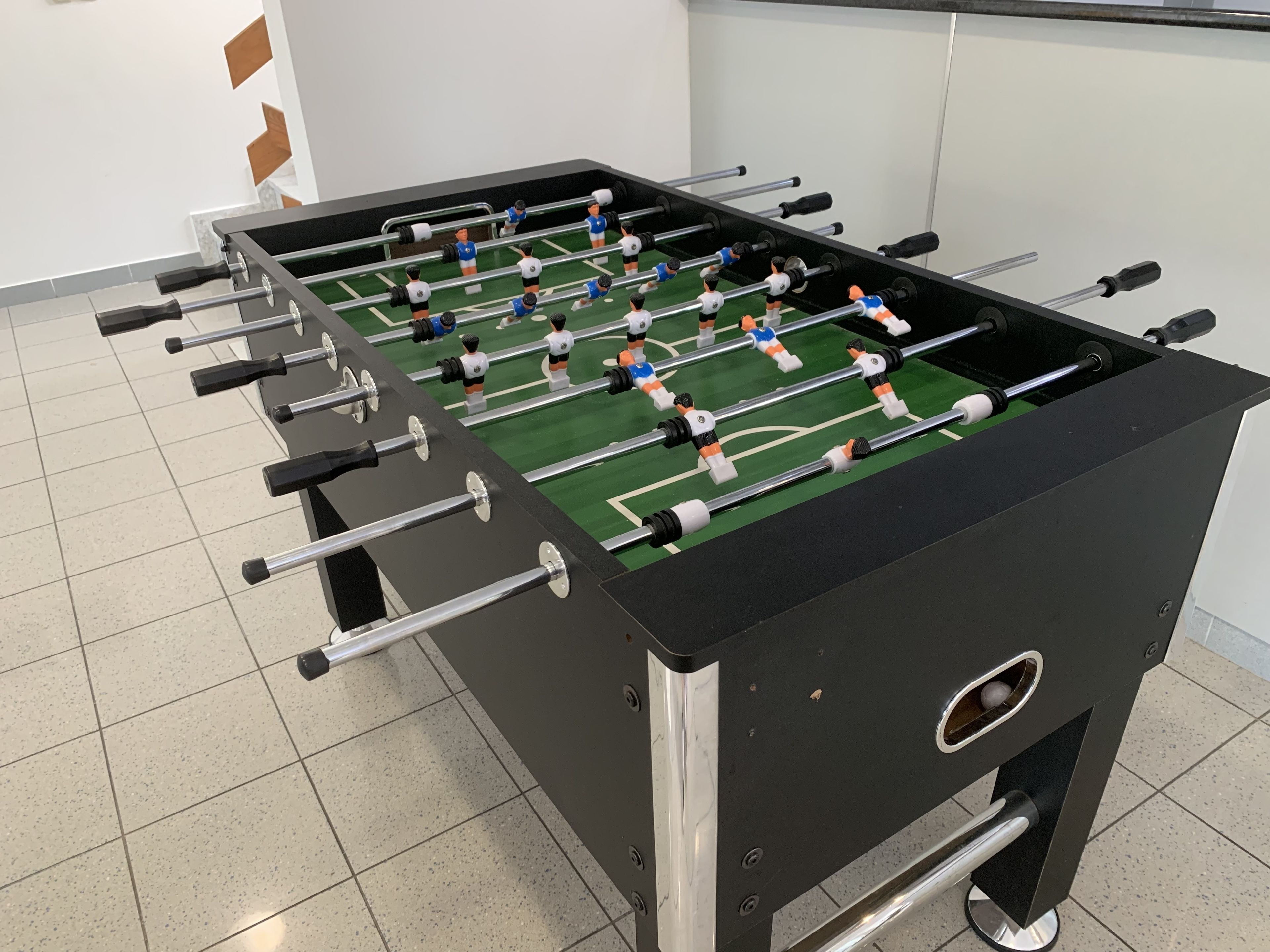 Een tafelvoetbaltafel met meerdere spelers en staven, op een betegelde vloer.