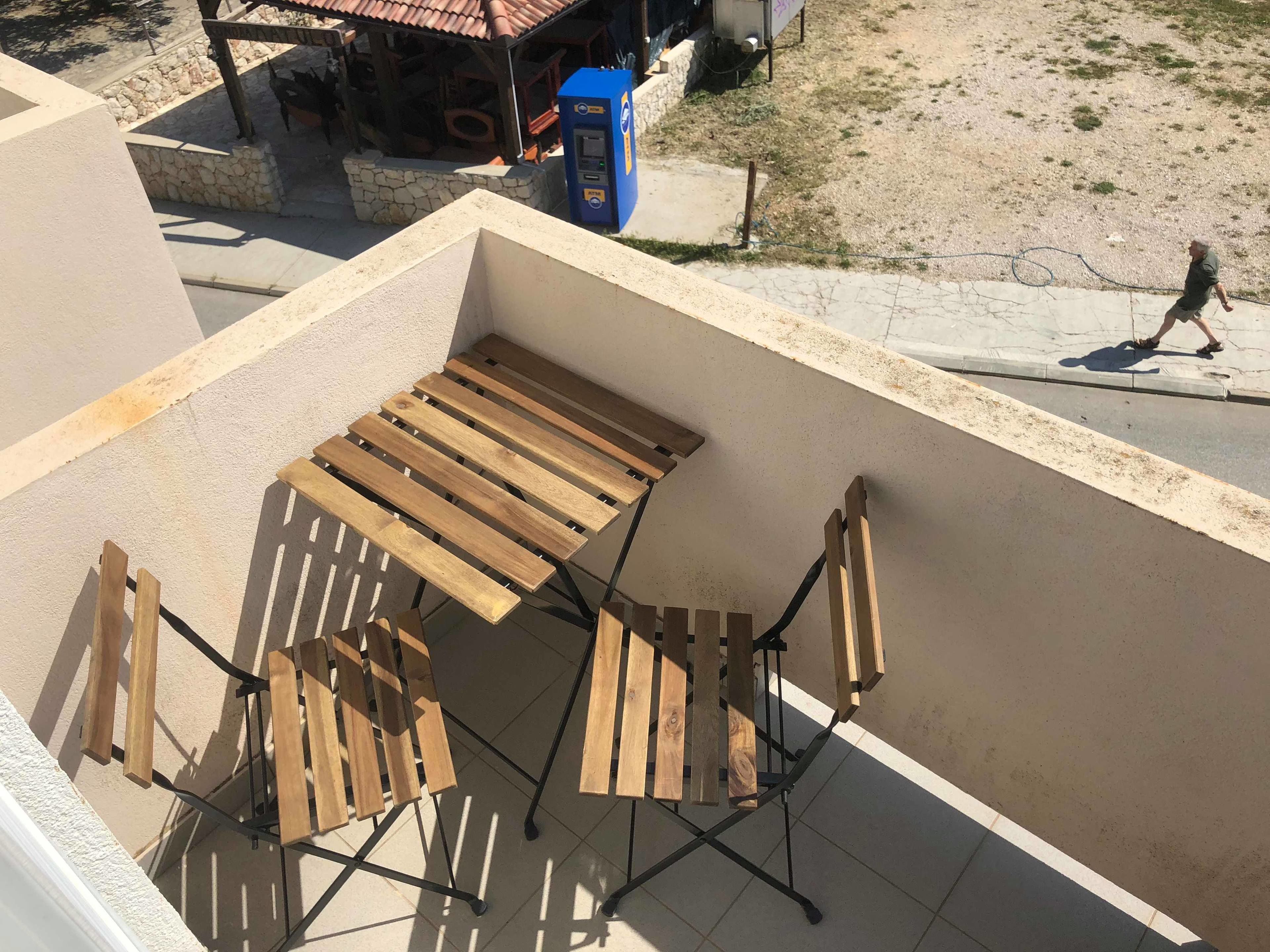 Terrassa al terrat amb taula i cadires de fusta, una màquina expenedora blava i una paret de pedra.