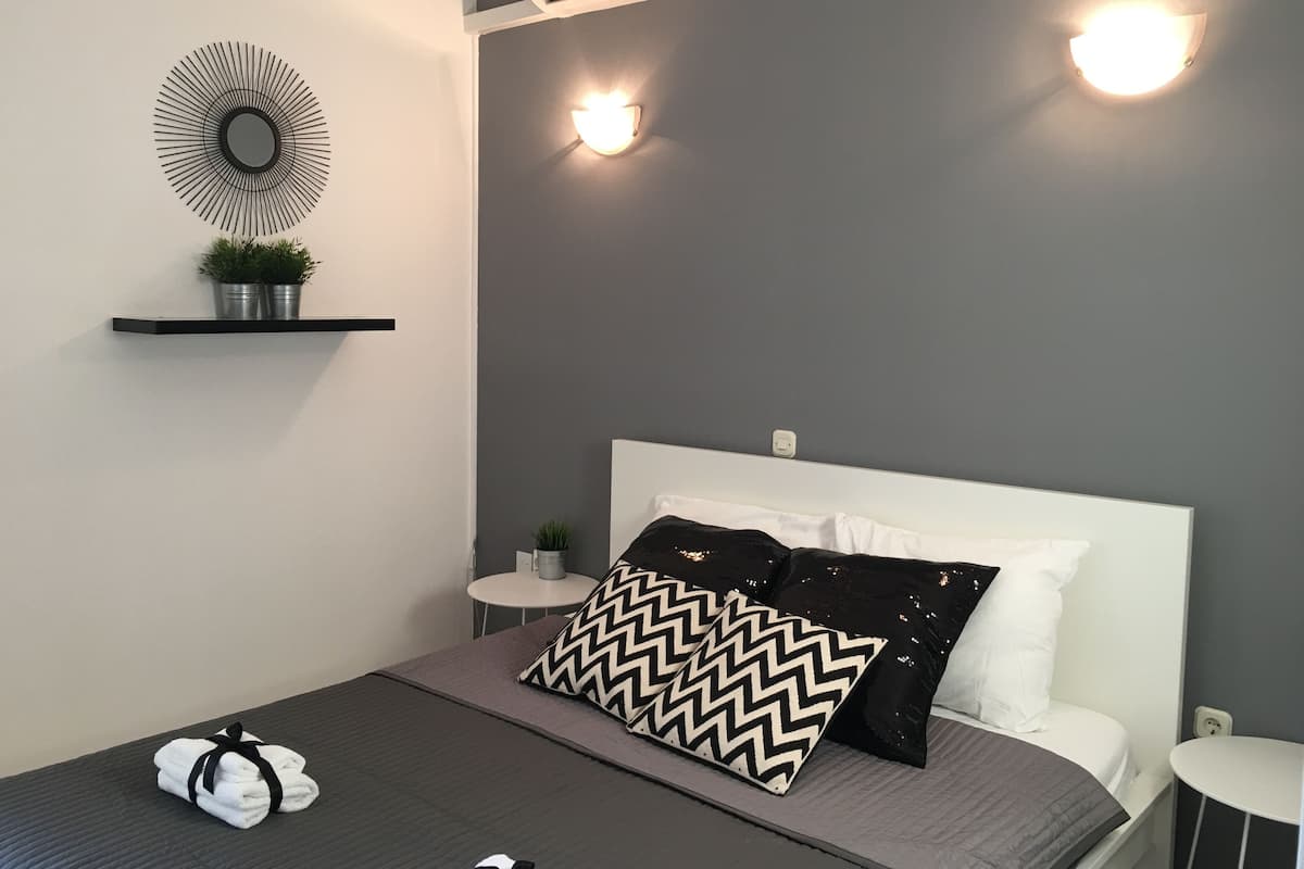 A modern bedroom with a bed, a wall-mounted air conditioner, a round mirror, and two wall sconces.
