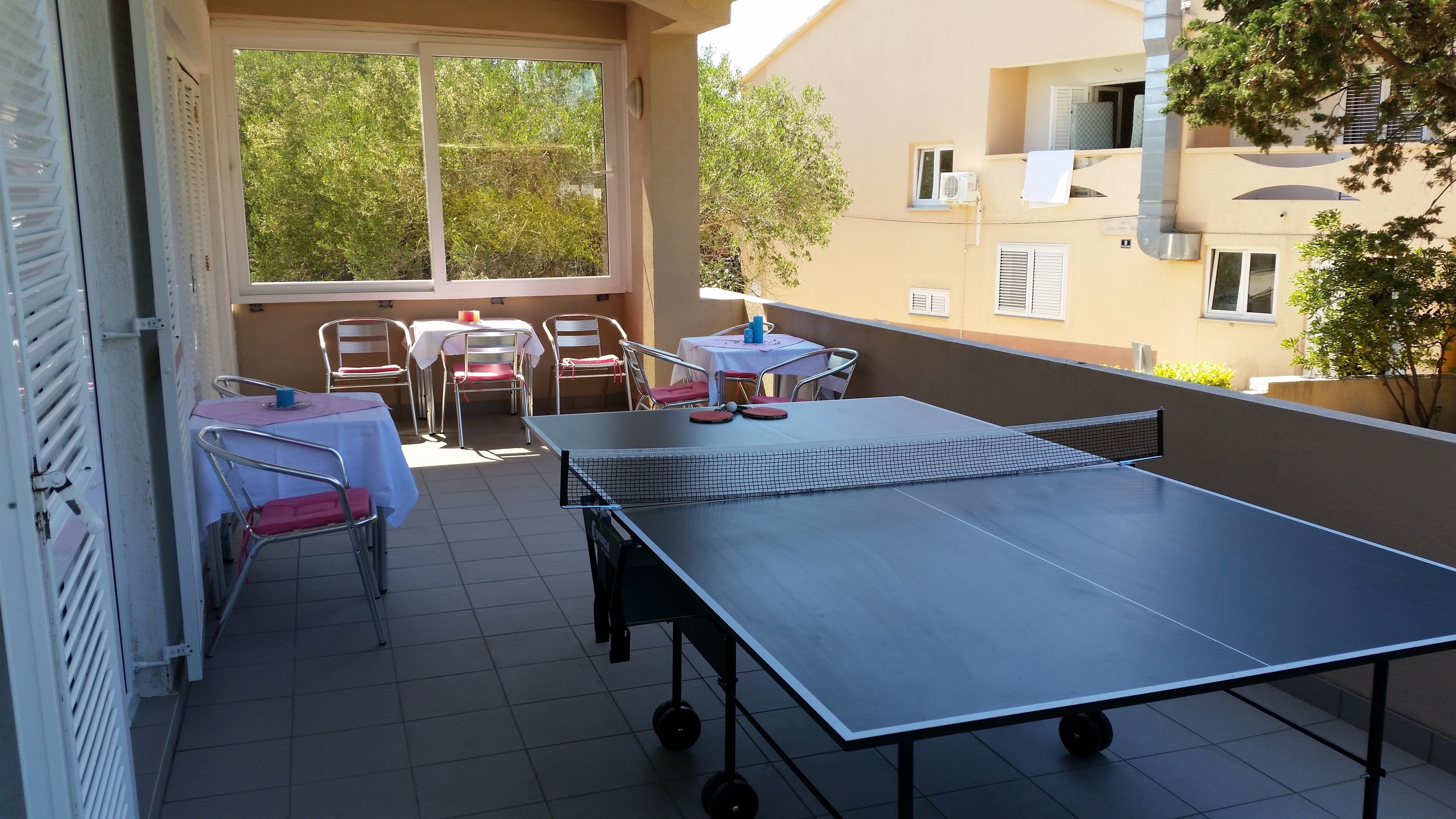 Een tafeltennisinstallatie buiten, met stoelen en een tafel, omringd door een gebouw met ramen en balkons.