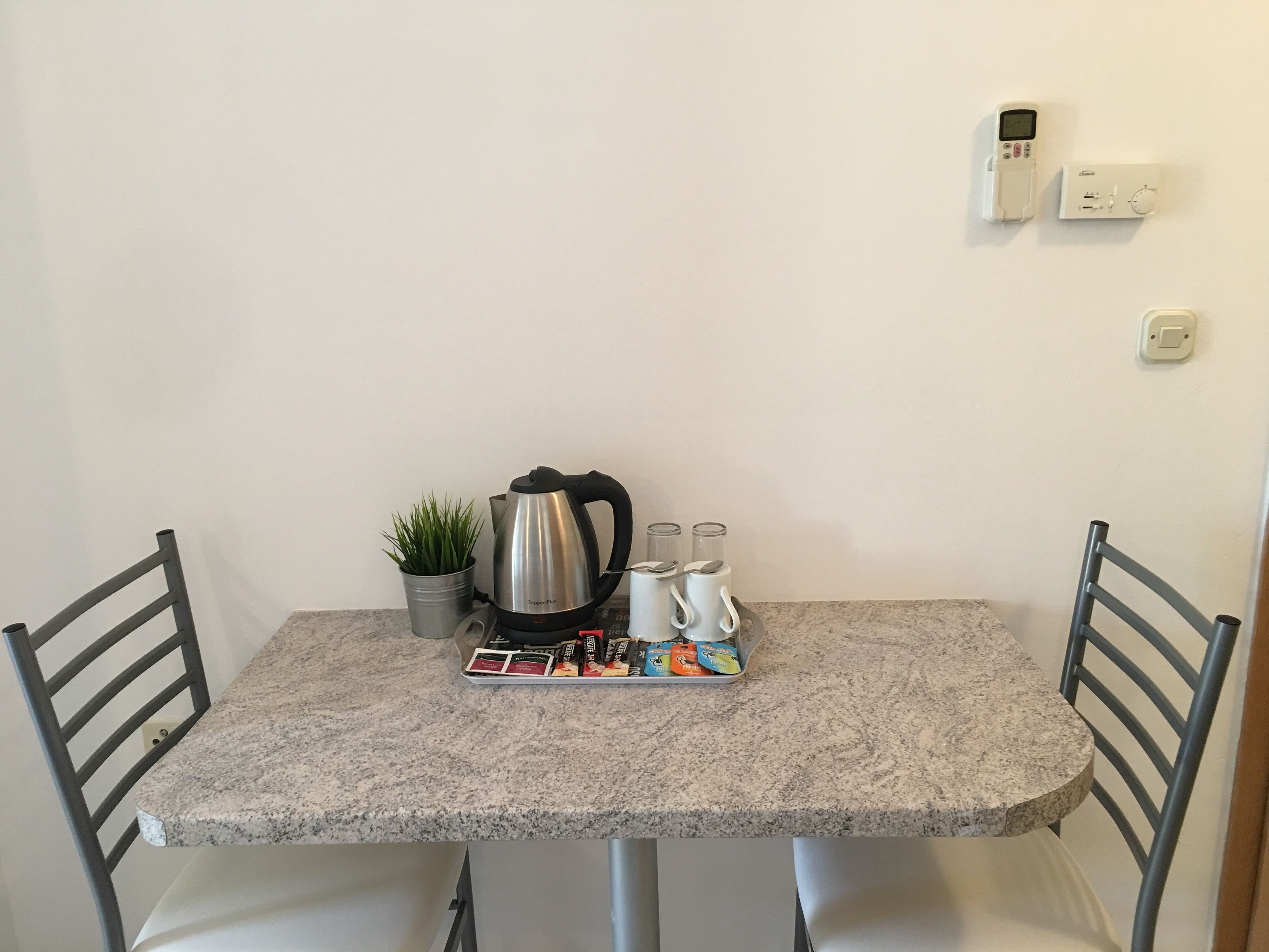 A small kitchen with a granite countertop, a kettle, a coffee maker, a plant, and a tray of coffee pods.