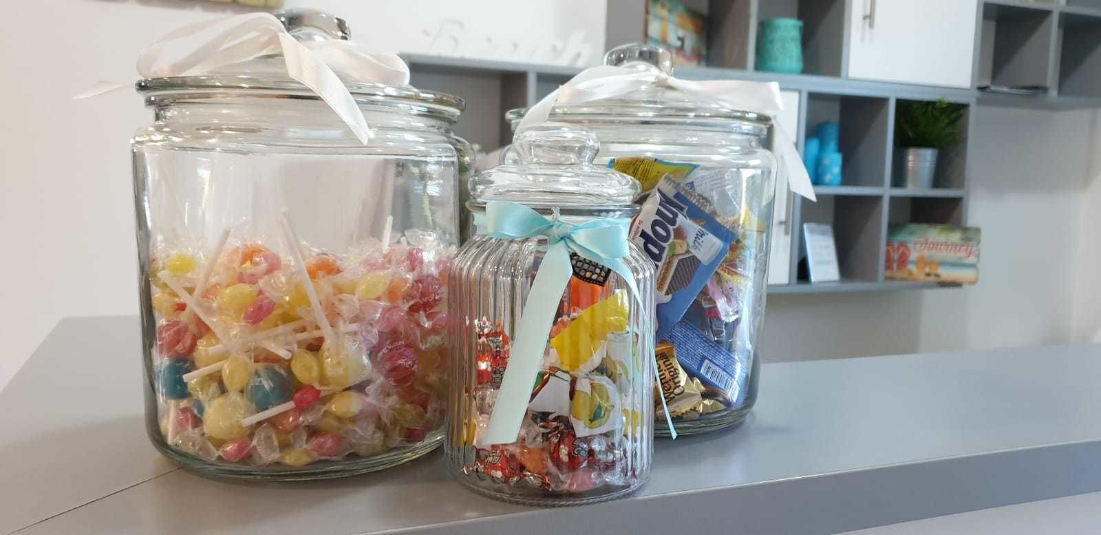Tres frascos de vidrio con caramelos y chocolates de colores, atados con cintas, sobre una estantería.