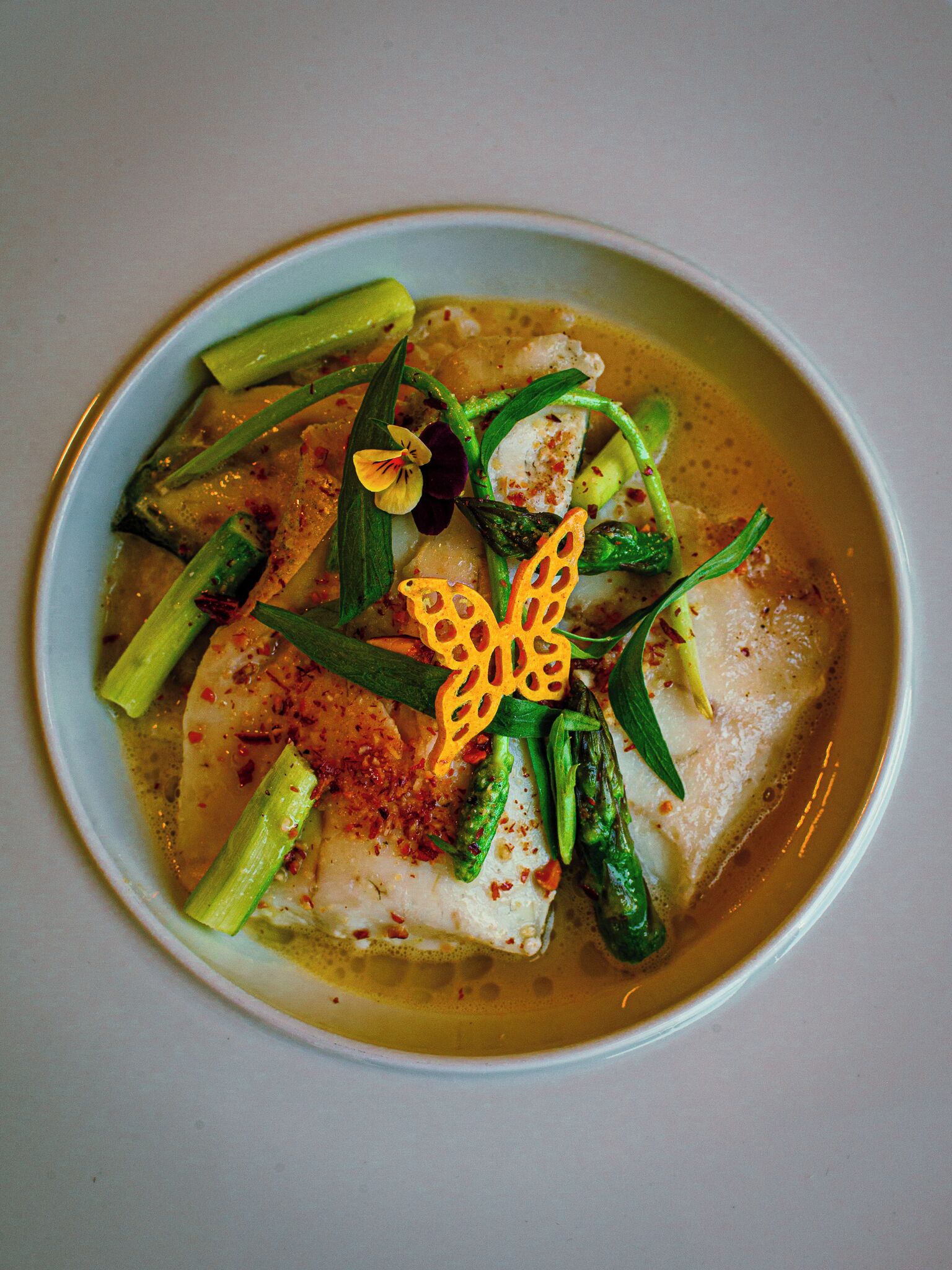 A bowl of fish with asparagus and a decorative flower.