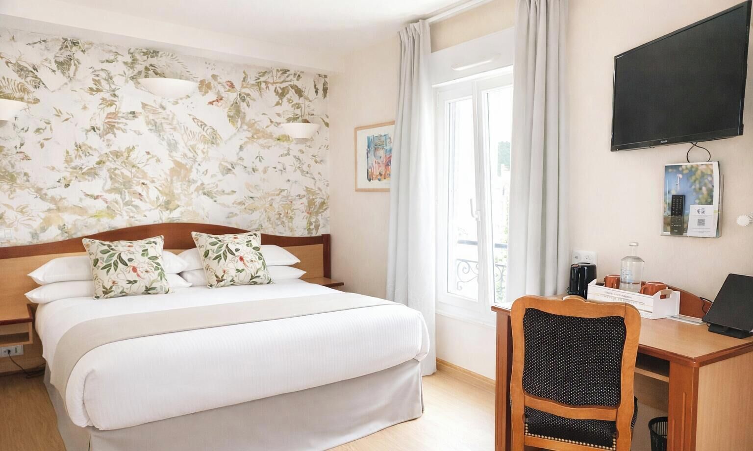 A hotel room with a bed, a desk, a chair, a TV, and a window with curtains.