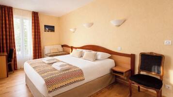A hotel room with a large bed, a chair, a nightstand, and a wall-mounted lamp.
