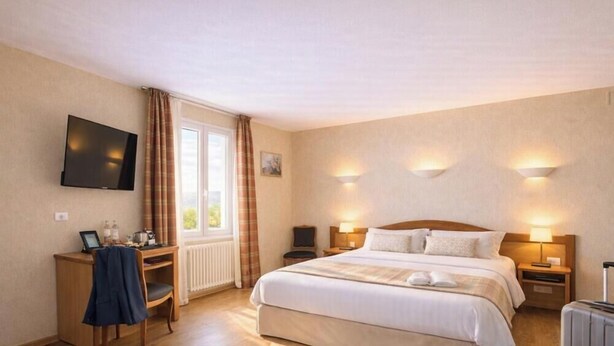 Habitación de hotel con cama, lámparas de noche, escritorio con silla, televisor montado en la pared y ventana con cortinas.