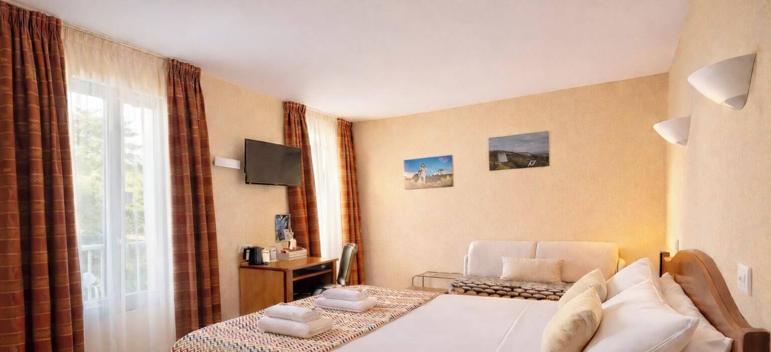 A hotel room with a bed, a desk, a chair, a TV, and two paintings on the wall.
