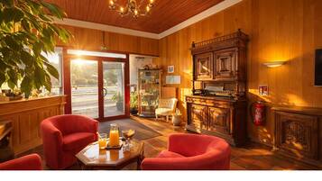 A wooden interior with a piano, red chairs, a glass table with drinks, and a large plant.