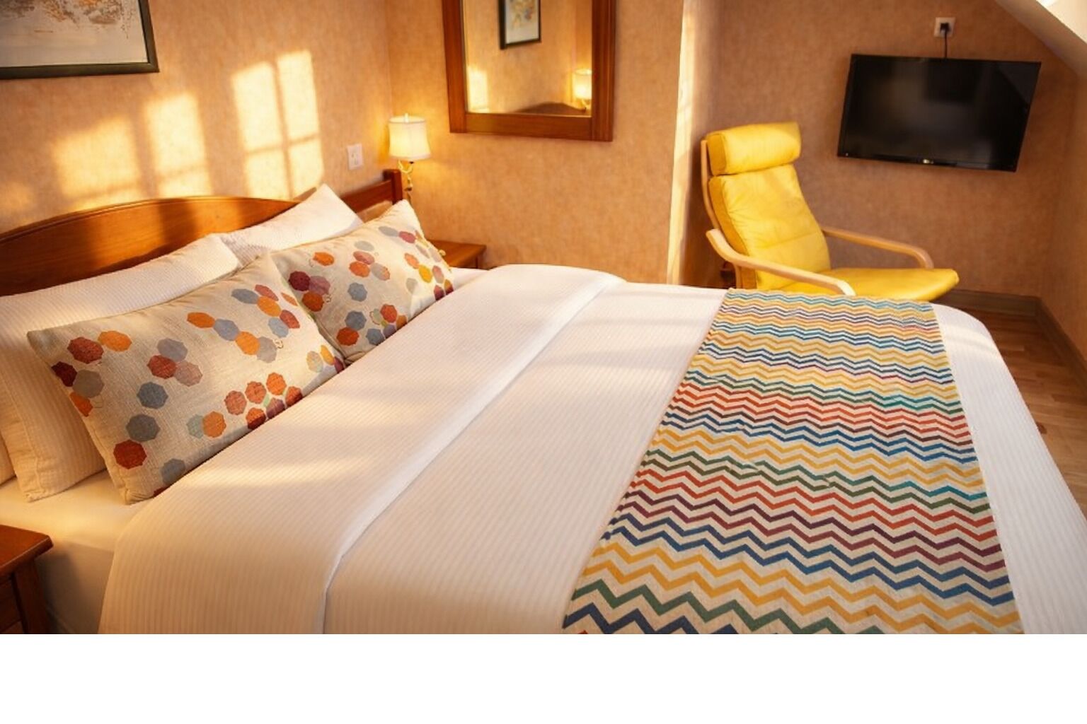 A hotel room with a bed, pillows, a chair, a TV, and a mirror.