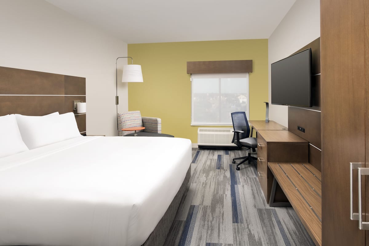 Habitación de hotel con una cama grande, un escritorio con silla, televisor y ventana con vistas.