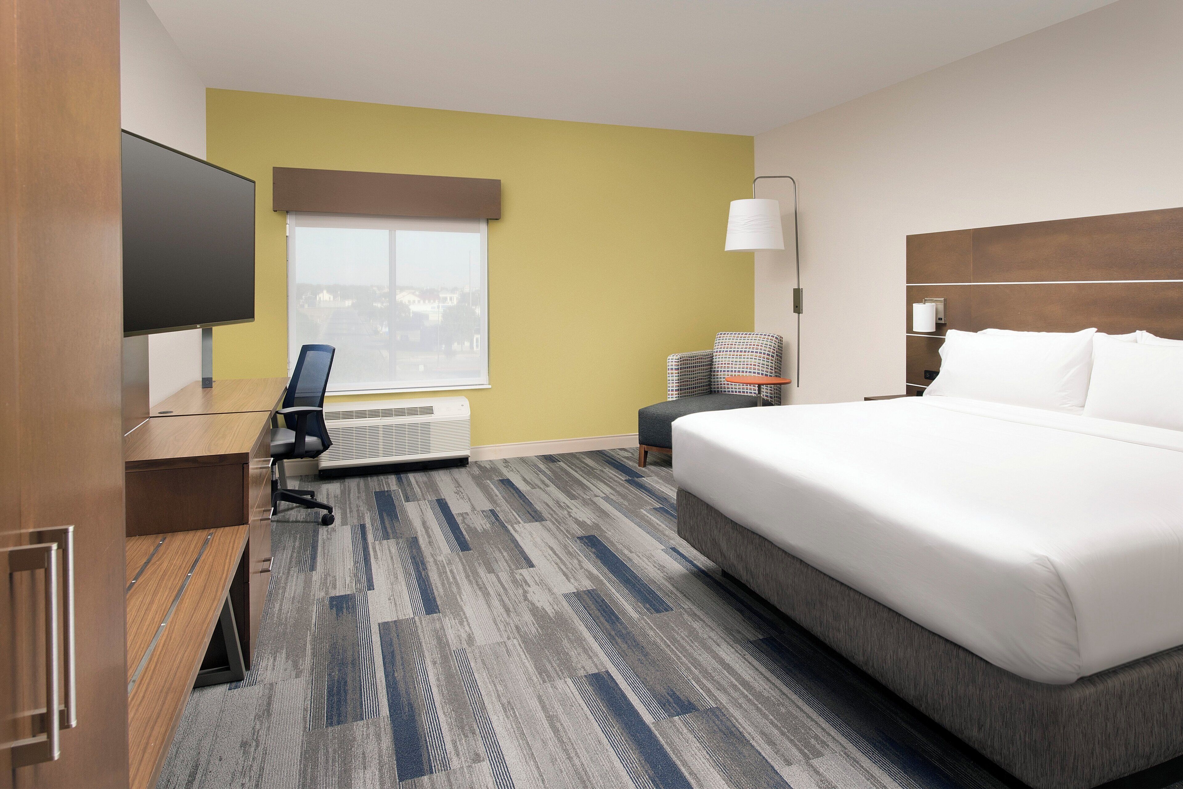 Ein Hotelzimmer mit Bett, Schreibtisch, Stuhl, Fernseher, Fenster und Lampe.