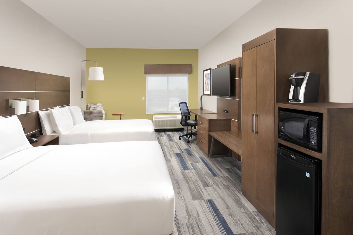 Habitación de hotel con dos camas, un escritorio, un televisor, un microondas y un refrigerador.