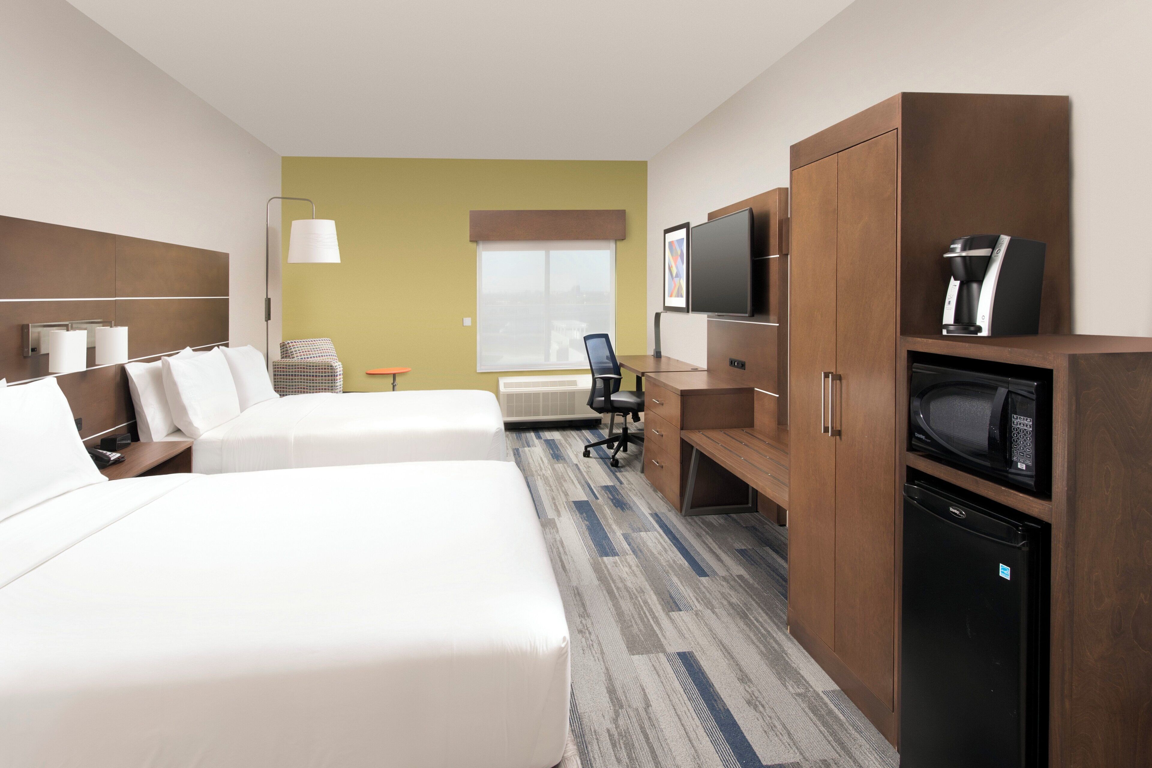 Habitación de hotel con dos camas, un escritorio, televisor y cafetera.