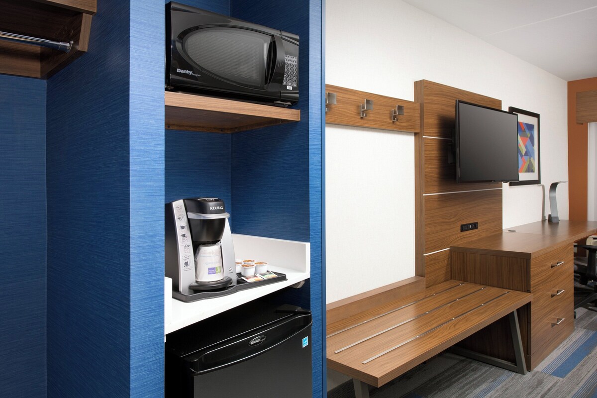 Habitación de hotel con microondas, cafetera y televisor de pantalla plana sobre un mueble de madera.