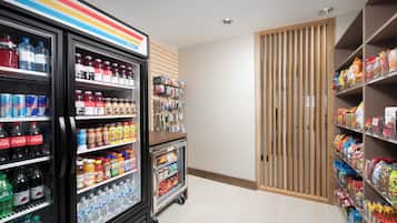 L’intérieur d’un magasin, avec des distributeurs de boissons réfrigérés, des étagères à collations et une porte en bois.