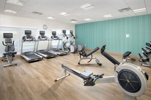 Un gimnasio con cintas de correr, elípticas y una máquina de remo.