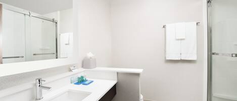 Un baño moderno con lavamanos blanco, espejo y cabina de ducha de vidrio.