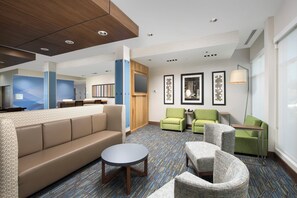 A hotel lobby with a sofa, chairs, a small table, a reception desk, and framed artwork on the walls. - Holiday Inn Express & Suites San Antonio North - Windcrest by IHG (San Antonio)
