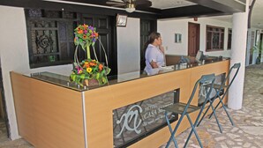 Bancada de recepção de hotel com tampo de vidro, um arranjo floral e uma placa com o nome do hotel.