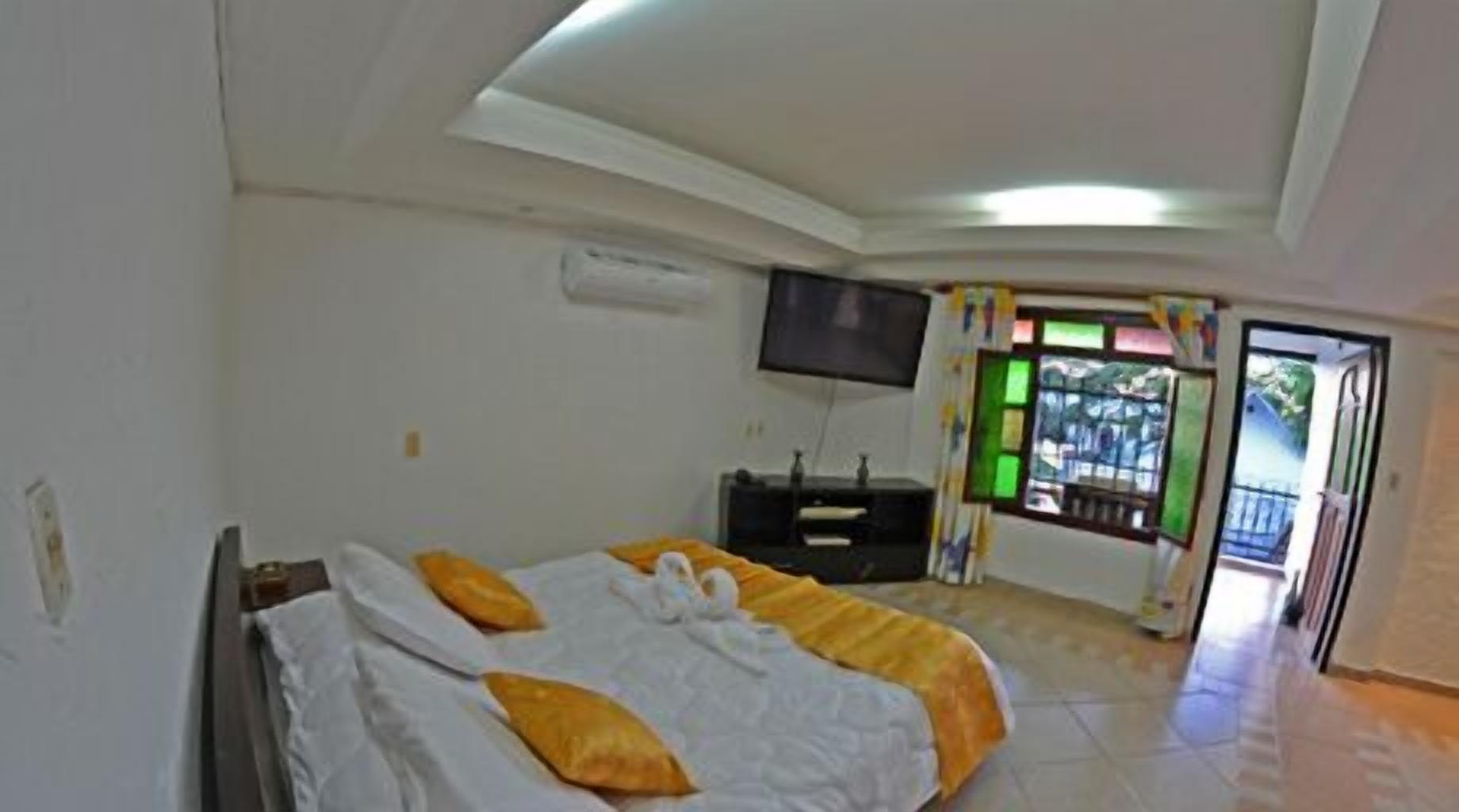 A hotel room with a bed, a flat-screen TV, a window with curtains, and a balcony.