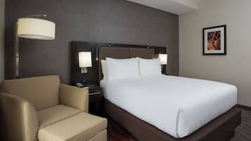 A hotel room with a bed, a chair, a nightstand, and a wall-mounted lamp.