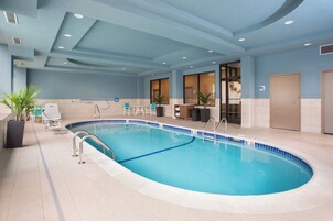 Una piscina interior con agua azul cristalina, rodeada de piso de baldosas y equipada con barandillas de seguridad.