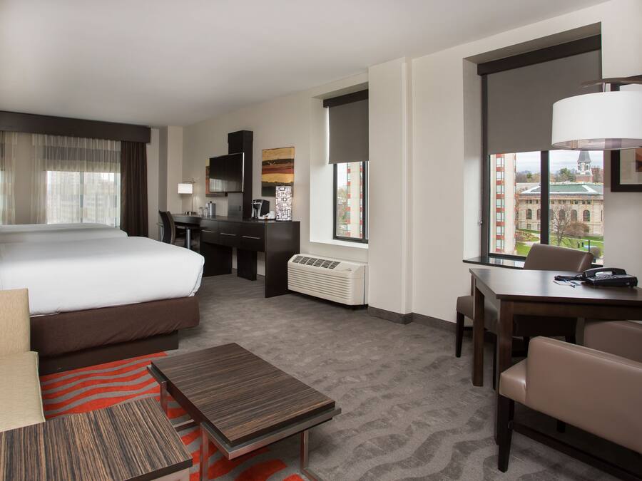 Habitación de hotel con cama, escritorio, silla, mesita y ventana con vista a un edificio.