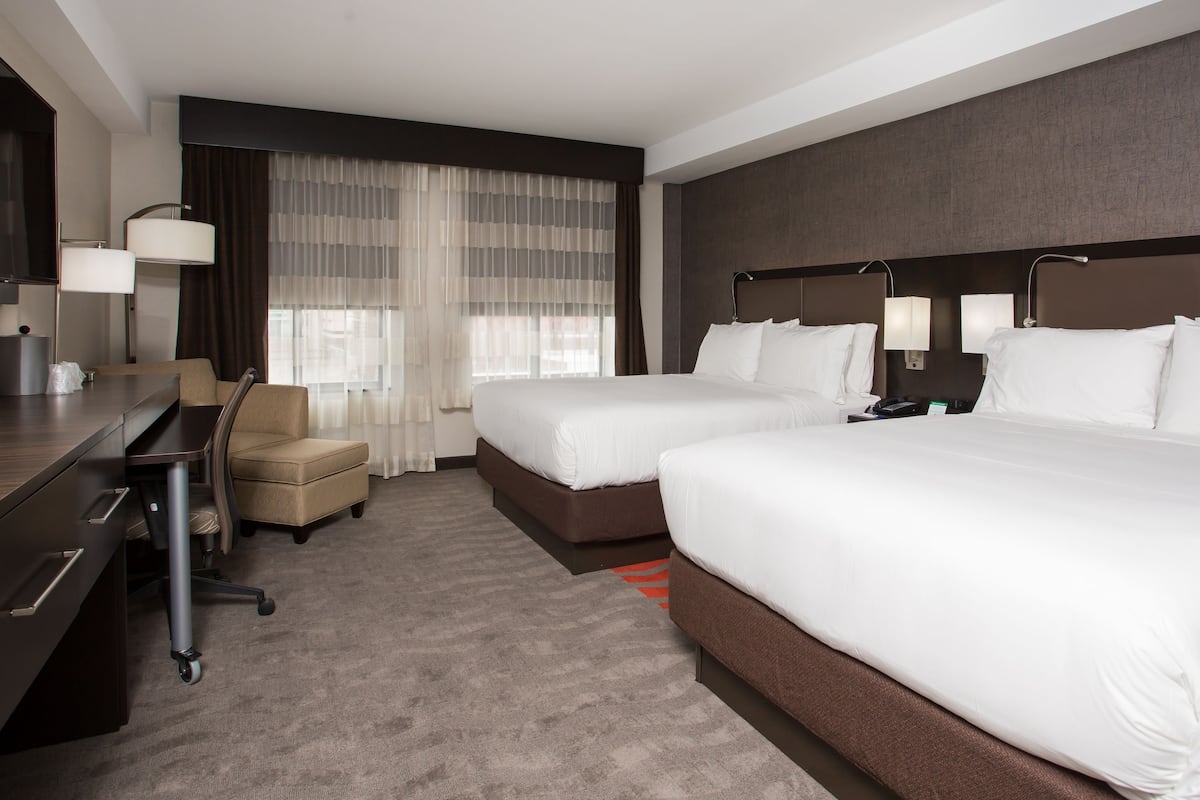 A hotel room with two beds, a desk, a chair, and a large window with curtains.