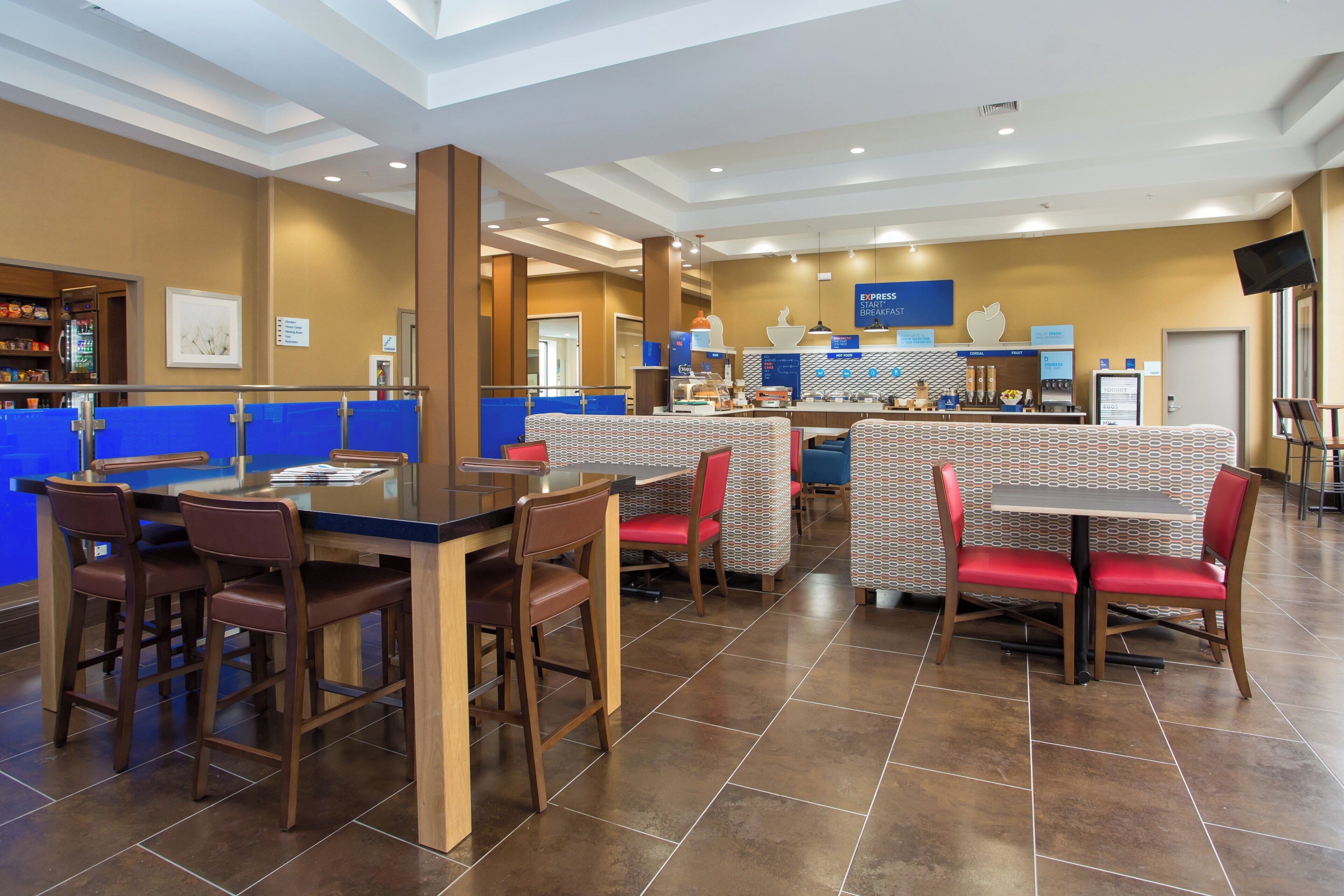 A hotel breakfast area with a counter, seating, and a wall displaying breakfast options.
