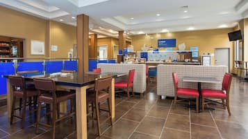 A hotel breakfast area with a counter, seating, and a wall displaying breakfast options.