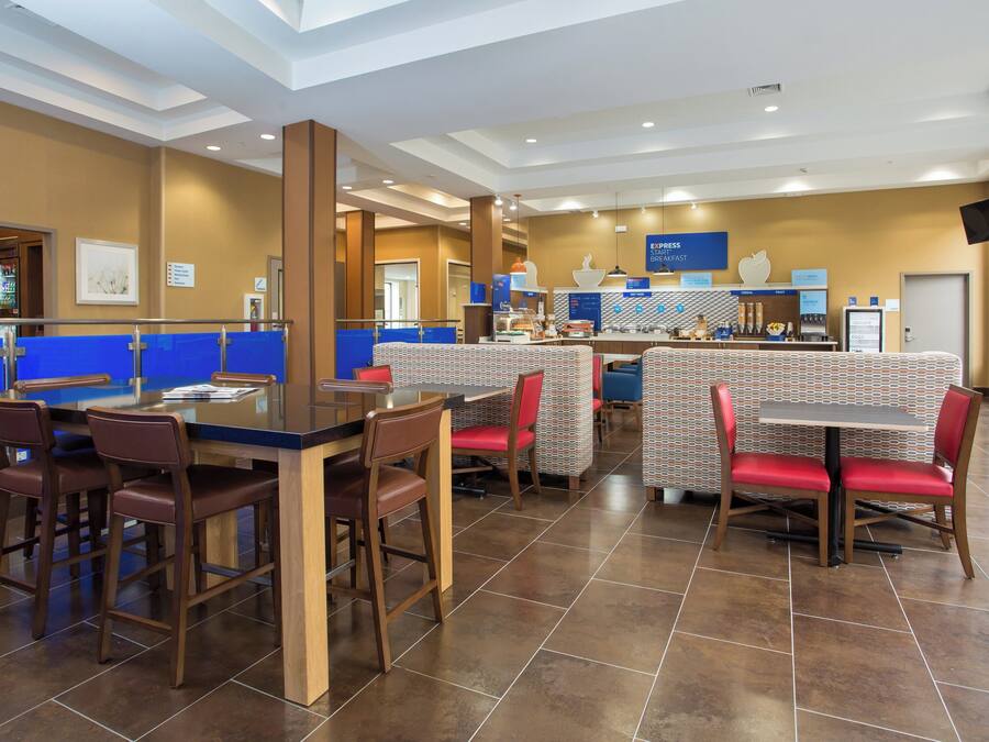 A hotel breakfast area with a counter, seating, and a wall displaying breakfast options.
