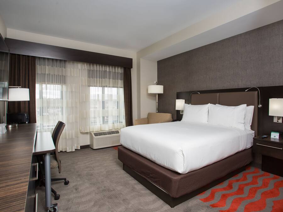 Une chambre d’hôtel avec un grand lit, un bureau et une chaise. On y trouve également une télévision, une lampe et une table de chevet avec un téléphone.