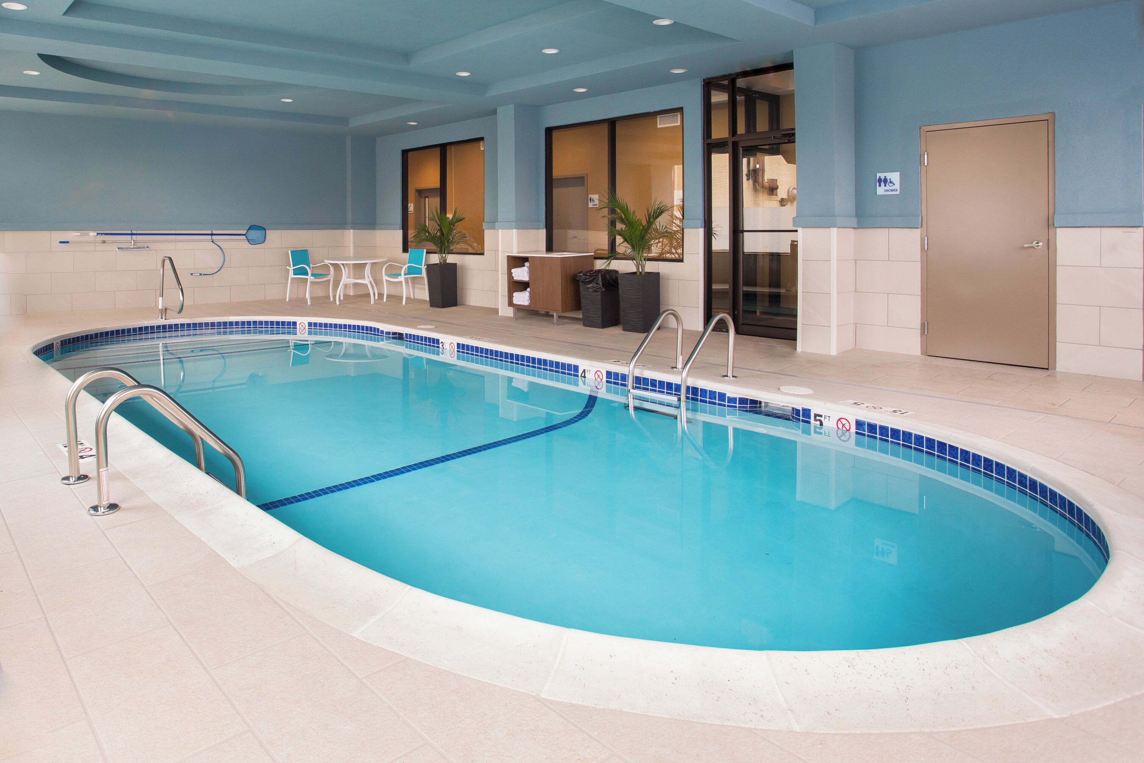 Ein Innenpool mit klarem, blauem Wasser, einer Poolleiter und einer Sitzgelegenheit mit Stühlen und einem Tisch.