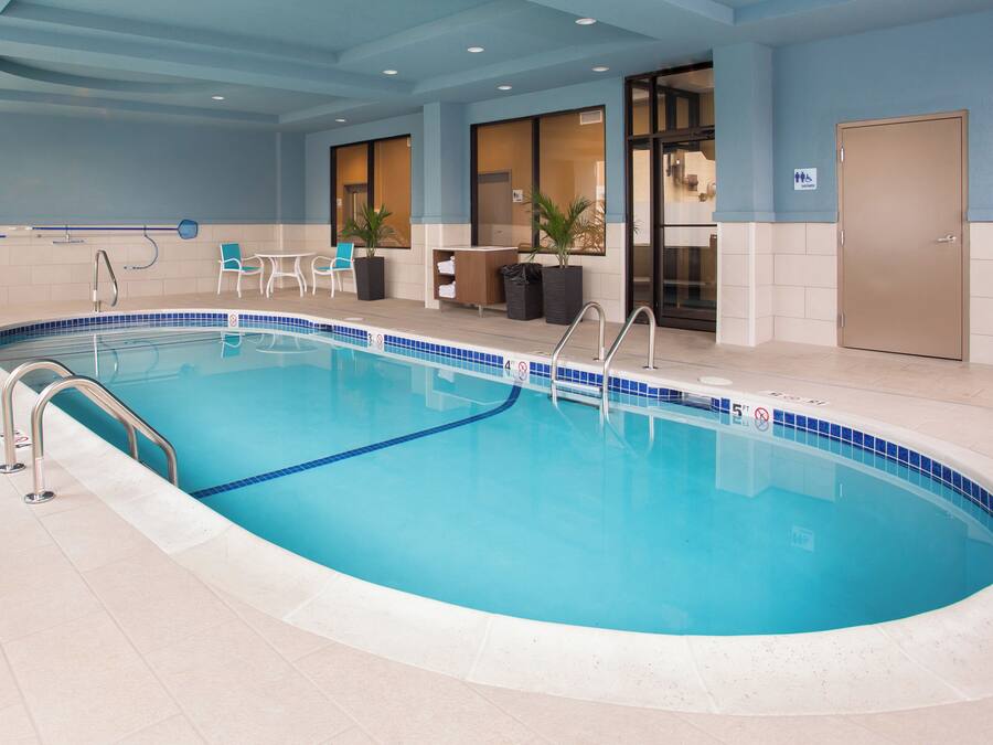 Une piscine intérieure à l’eau d’un bleu cristallin, avec un escalier et un espace détente comprenant des chaises et une table.