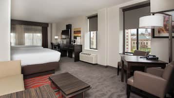 A hotel room with a bed, desk, chair, and a view of a building through the window.