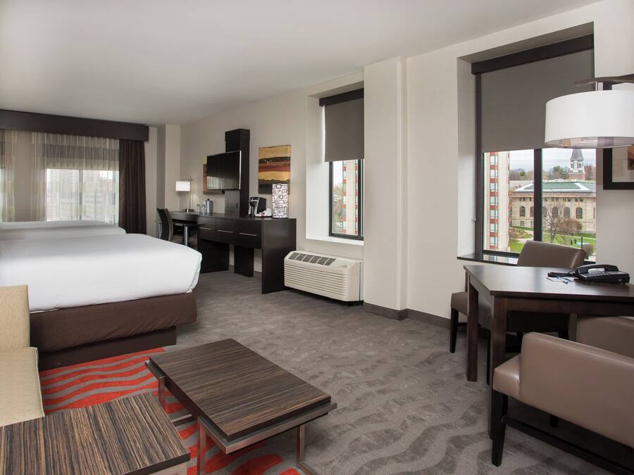 Habitación de hotel con cama, escritorio, silla y vista a un edificio a través del ventanal.