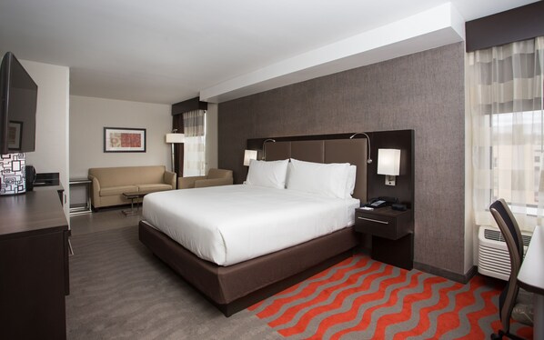 A hotel room with a large bed, a desk, a chair, and a sofa.