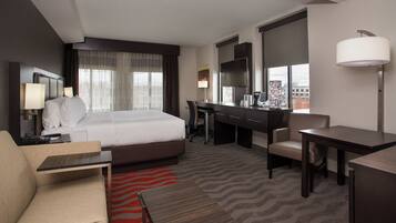 A hotel room with a bed, desk, chair, and a view of the city.