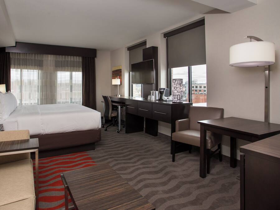 A hotel room with a bed, desk, chair, and a view of the city.