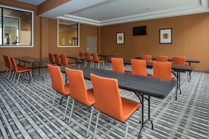 Une salle de conférence dotée de plusieurs tables et de chaises orange, d’un sol recouvert de moquette et de tableaux encadrés accrochés aux murs.