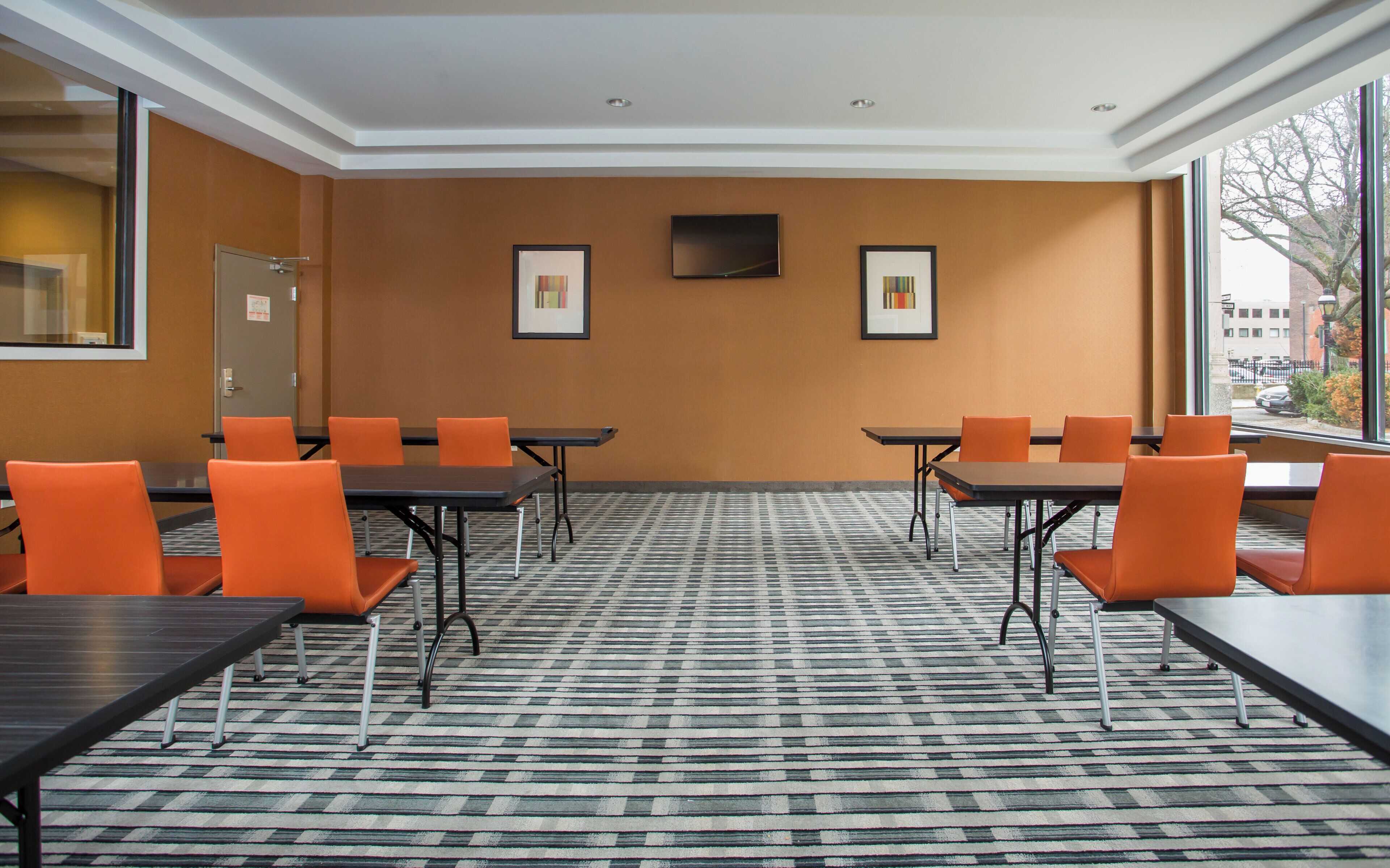 A conference room with tables and chairs, a flat-screen TV, and framed artwork on the wall.